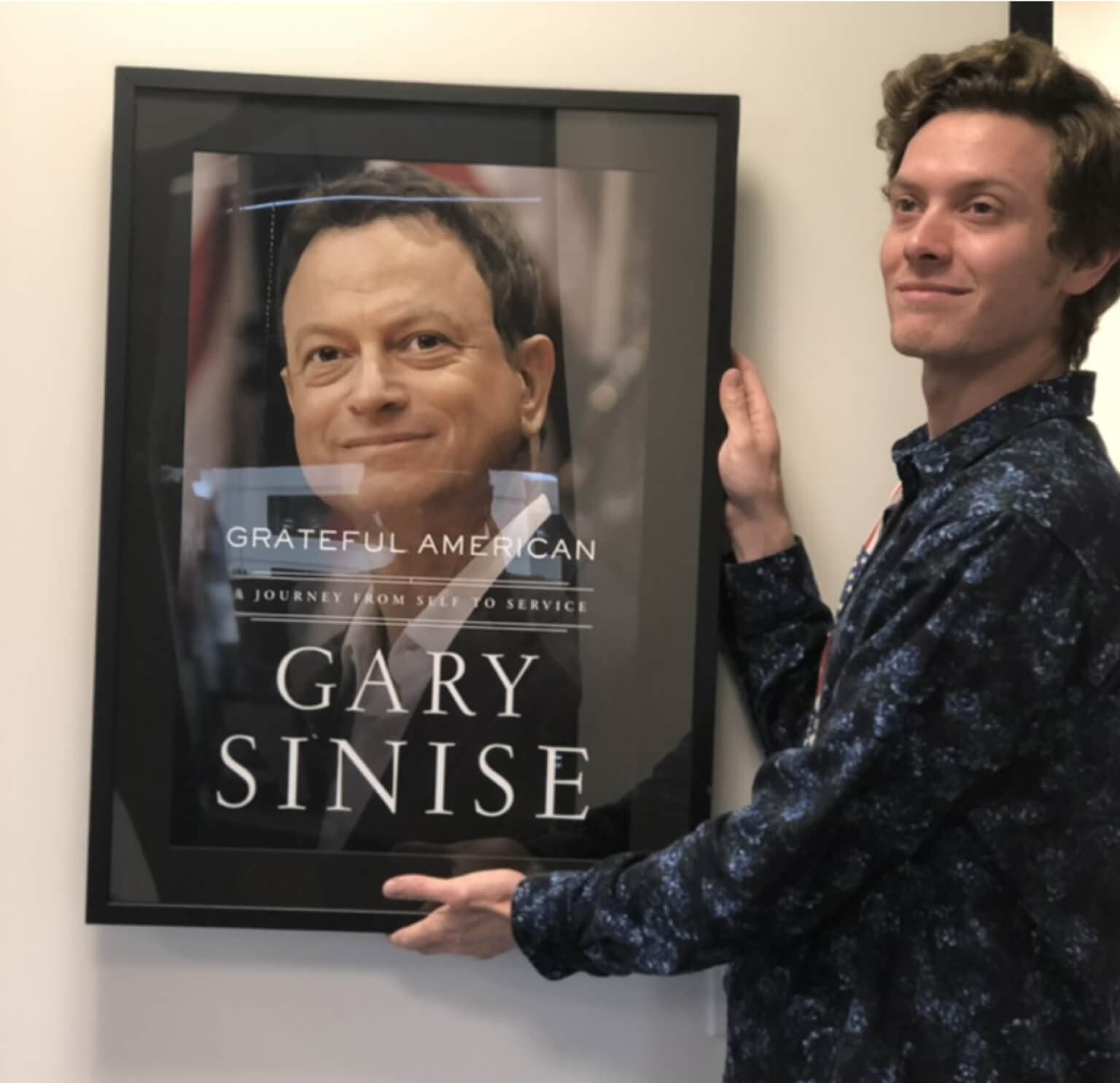 Mac holding a poster of his father's book cover, Grateful American, A Journey From Self to Service